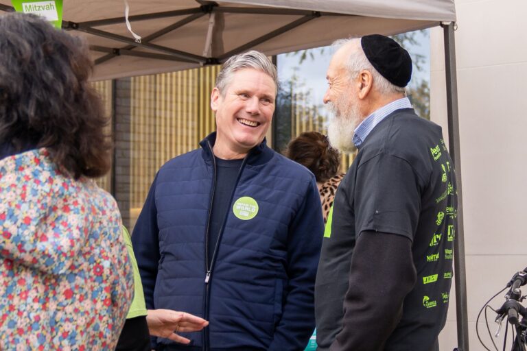 Keir Starmer laughing with a man while wearing a sticker saying 'repair the world'