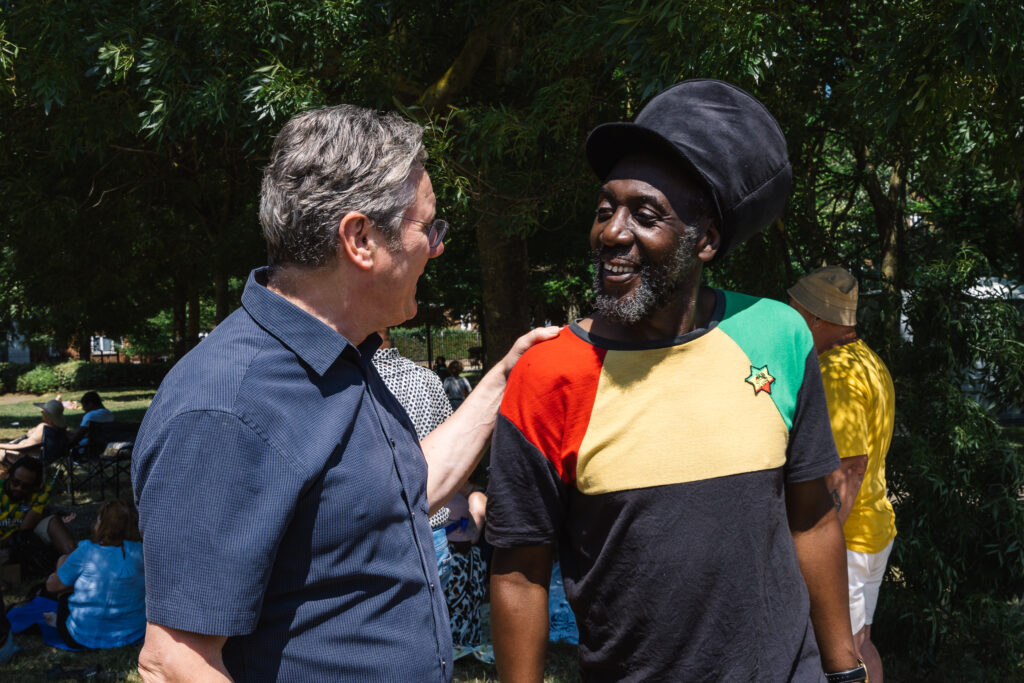 Keir Starmer, standing with his hand on a man's shoulder, in front of trees