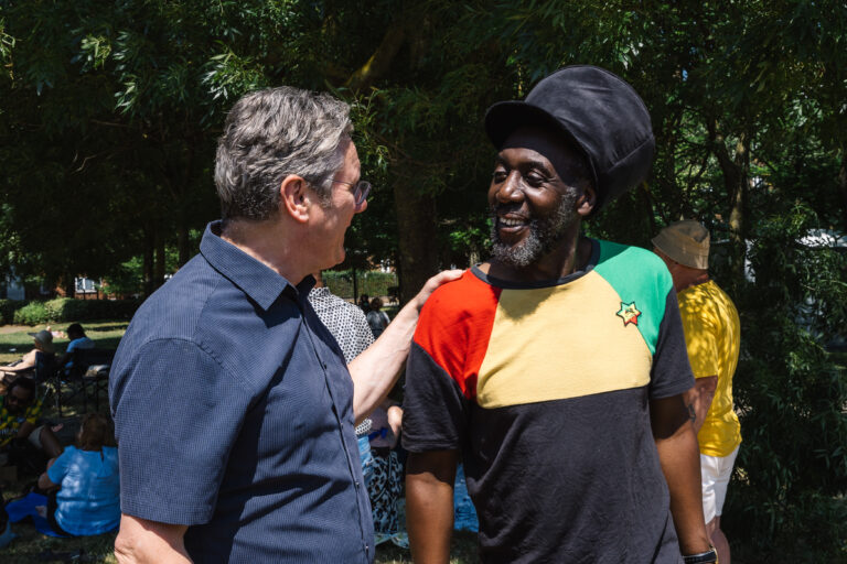 Keir Starmer, standing with his hand on a man's shoulder, in front of trees