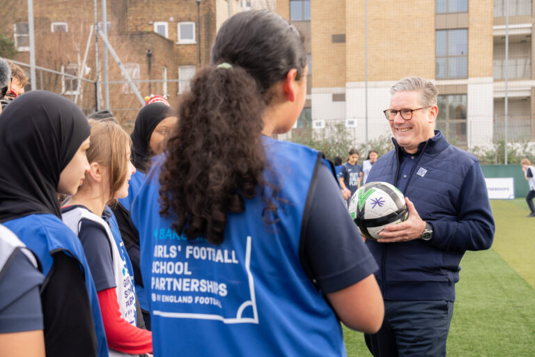 Keir Starmer is holding a football and talking to a group of girls in football kit